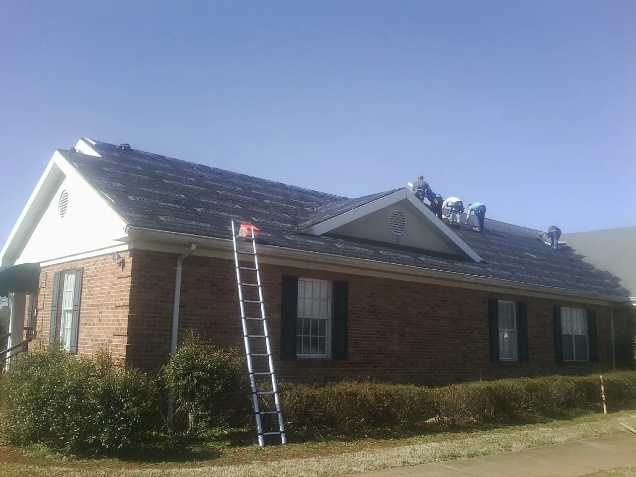 Crew tearing shingles off a brick ranch roof with a ladder set — Metal Roof Repair work by our crew in La Fayette